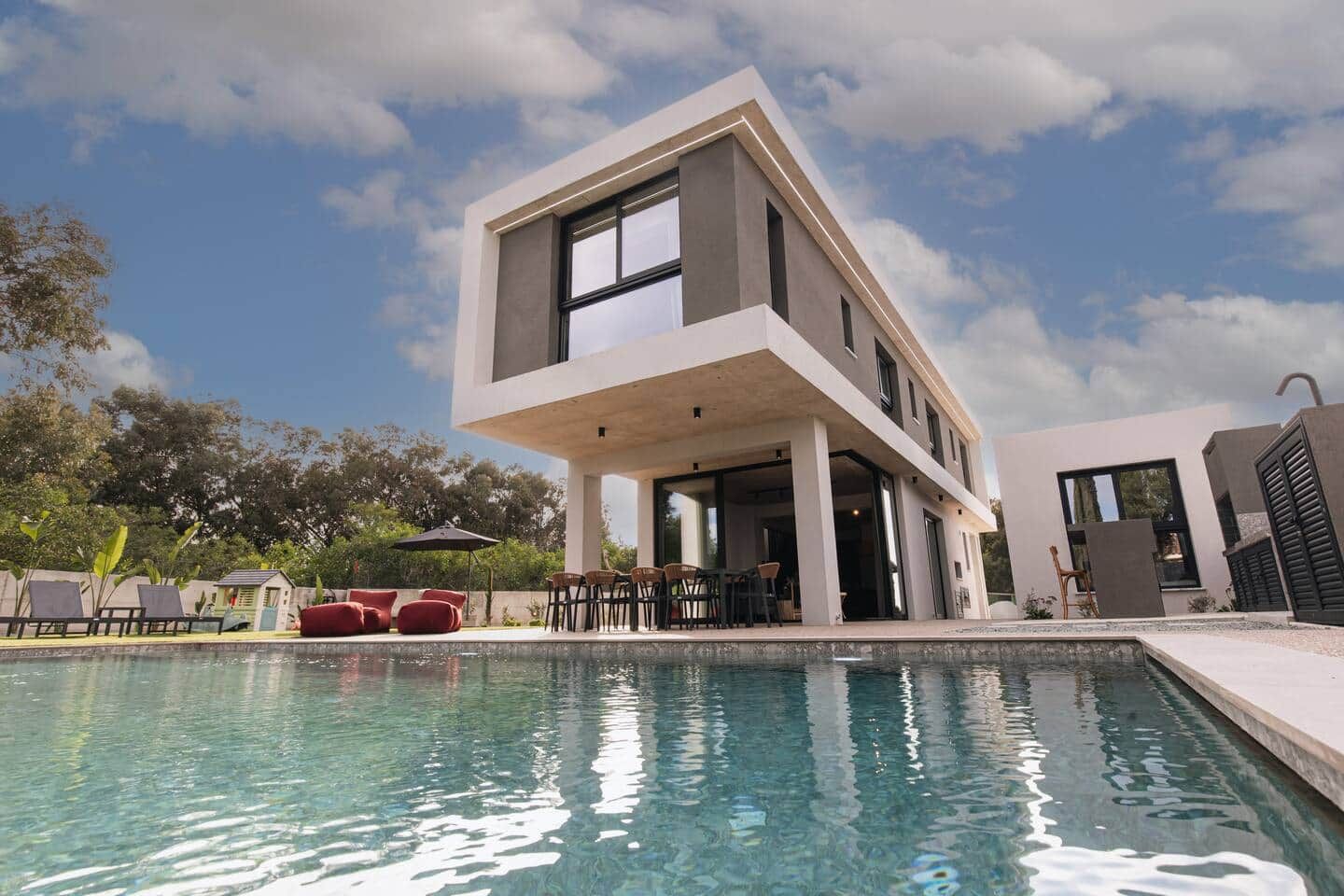 A modern two-story house with a pool, outdoor seating, and a clear sky.