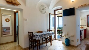A dining area with a table and chairs, a clock on the wall, and a view of the outside. - Terrazza Bella Vista by Interhome (Lingueglietta)