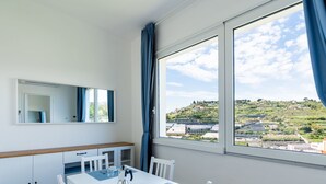 A modern dining area with a white table, chairs, and a view of a hilly landscape through large windows. - Calipso by Interhome (Sanremo)