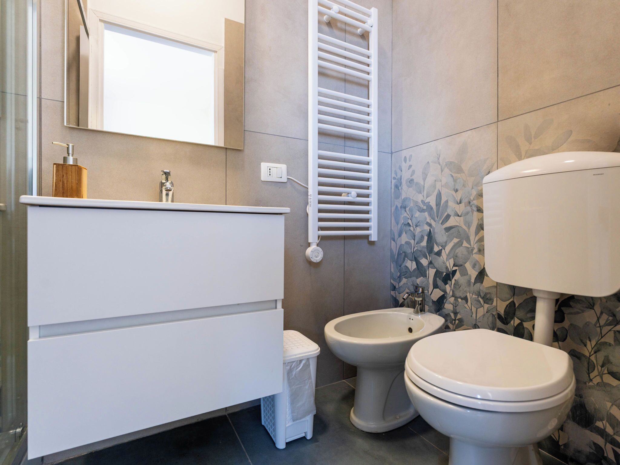 Een moderne badkamer met een witte wastafel, twee wasbakken, een toilet en een handdoekhouder.