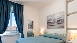 A bedroom with a bed, a window with curtains, a bedside table with a lamp, and a painting on the wall. - Calipso by Interhome (Sanremo)
