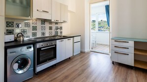 A modern kitchen with a washing machine, oven, and sink. There is a view of a balcony with a blue curtain. - Calipso by Interhome (Sanremo)