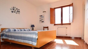 A bedroom with a wooden bed, a radiator, a window with wooden shutters, and a wall decoration. - Villa with large garden (Marina di Campo)