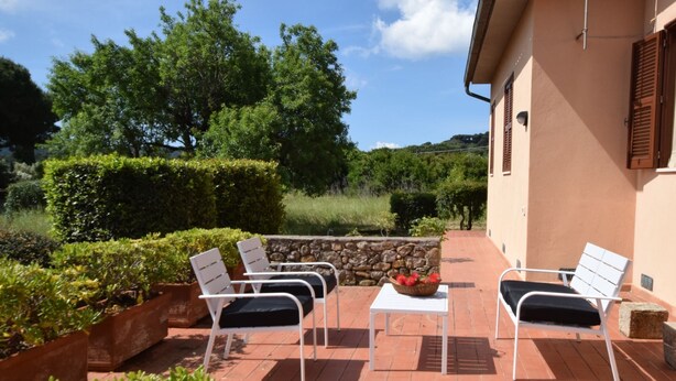A patio with white chairs and a table, surrounded by greenery and a stone wall. - Villa with large garden (Marina di Campo)