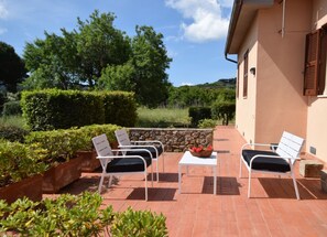 Eine Terrasse mit weißen Stühlen und einem Tisch, umgeben von Grünpflanzen und einer Steinmauer.
