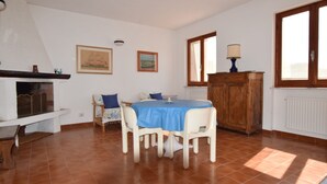 A dining area with a table set for four, surrounded by white chairs, a wooden cabinet, and a fireplace. - Villa with large garden (Marina di Campo)