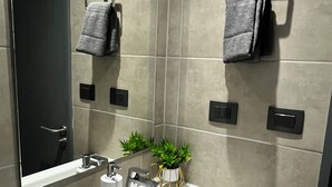 Un baño moderno con un lavamanos blanco, dos toalleros, un espejo y una pequeña planta en maceta.
