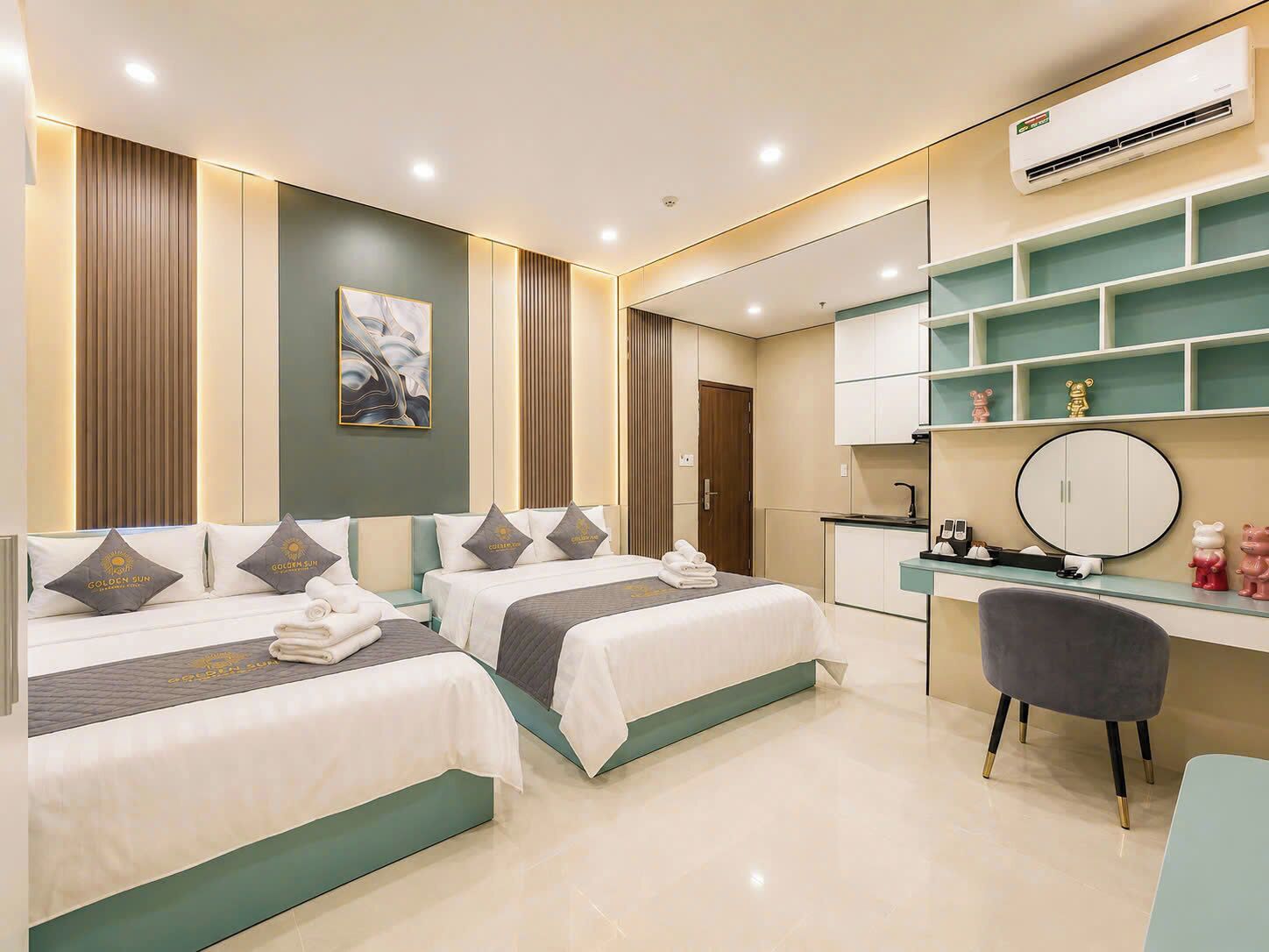 A hotel room with two beds, a desk, a chair, a mirror, and a built-in air conditioning unit.