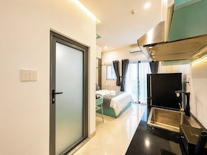 A modern hotel room with a bed, a desk, a refrigerator, and a sliding door.