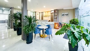 A modern hotel lobby with a marble reception desk, blue chairs, and large potted plants. - Golden Sun Hotel Apartments 5 (Ho Chi Minh City)