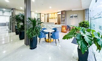 Un moderno vestíbulo de hotel con un mostrador de recepción de mármol, sillas azules y grandes plantas en macetas.