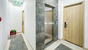 A hallway with a marble floor, an elevator, and a wooden door. - Golden Sun Hotel Apartments 5 (Ho Chi Minh City)