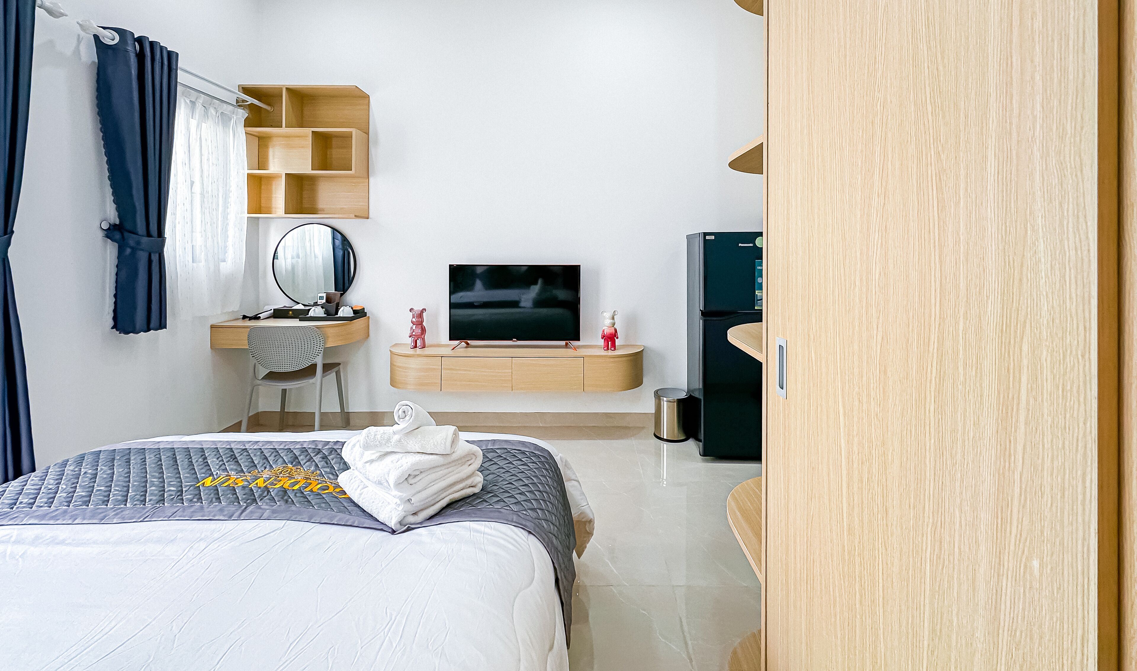 Una habitación de hotel con cama, televisión, escritorio con espejo, estante y armario.