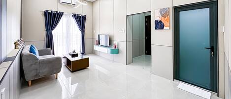 Una sala de estar moderna con un sofá, una mesa de centro, un televisor y un ventanal de vidrio que da a otra habitación.