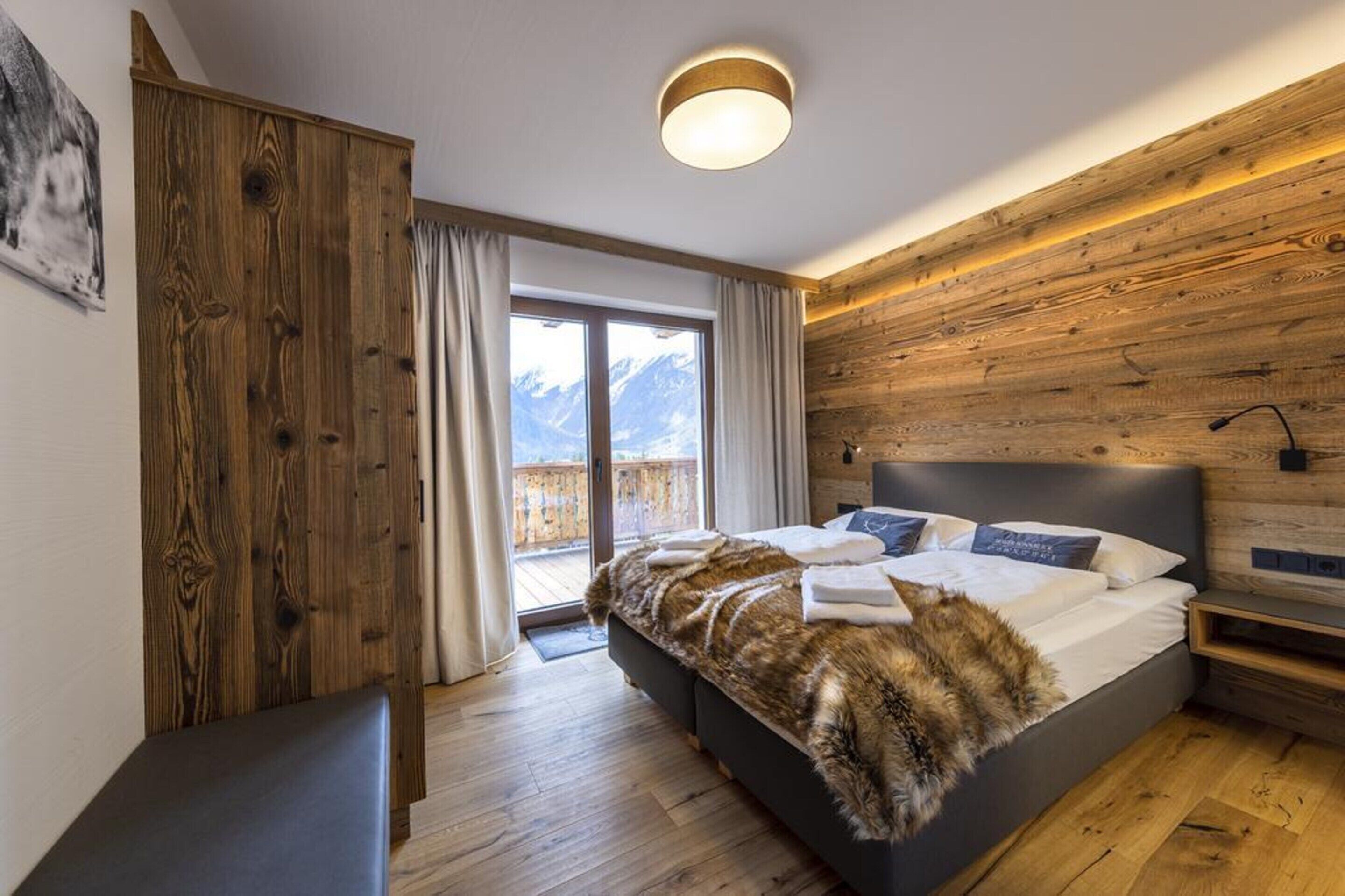 Un dormitorio con una cama grande, paredes de madera, un balcón con vistas a la montaña y una puerta corredera.