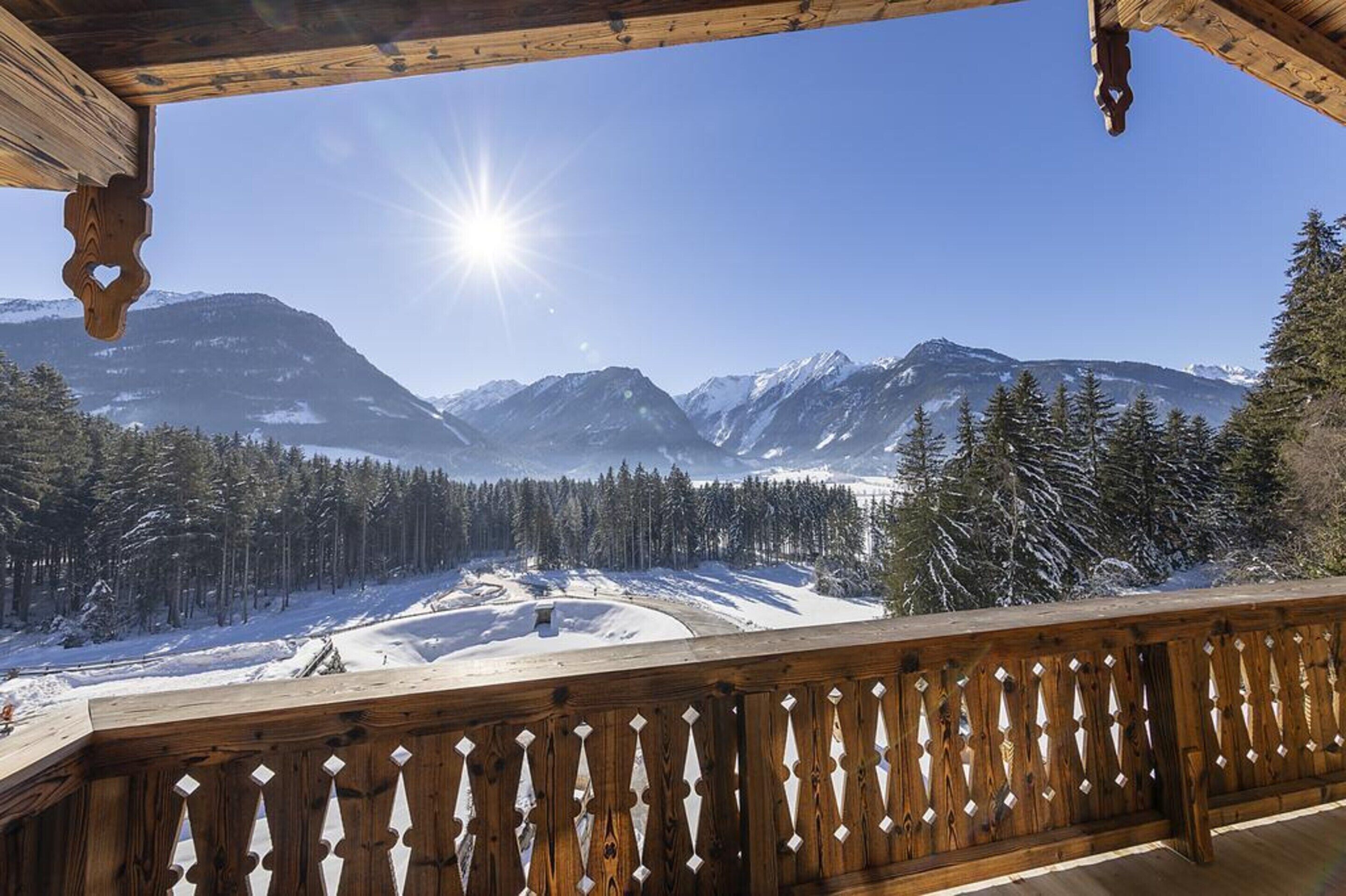 A wooden balcony with a view of snow-covered mountains and a clear sky.