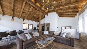 Ein großzügiger Wohnbereich mit Holzbalkendecke, einem großen Ecksofa, einem Glastisch und einem Essbereich mit Holztisch und Stühlen.