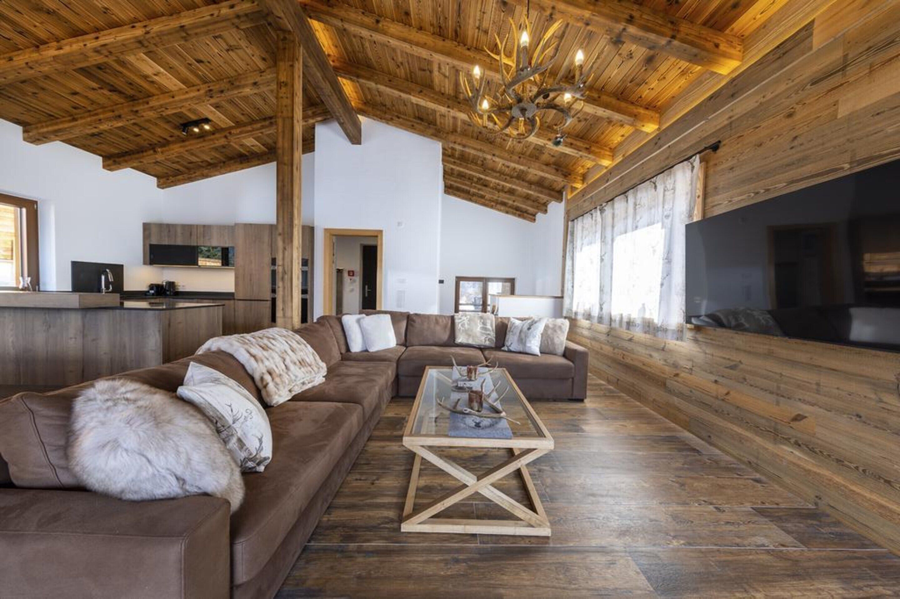 A spacious living area with a wooden ceiling, a large sofa, a coffee table, and a fireplace.