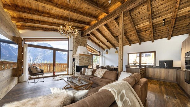 Ein geräumiges Wohnzimmer mit Holzboden, einem großen Sofa, einem Kamin und Bergblick.