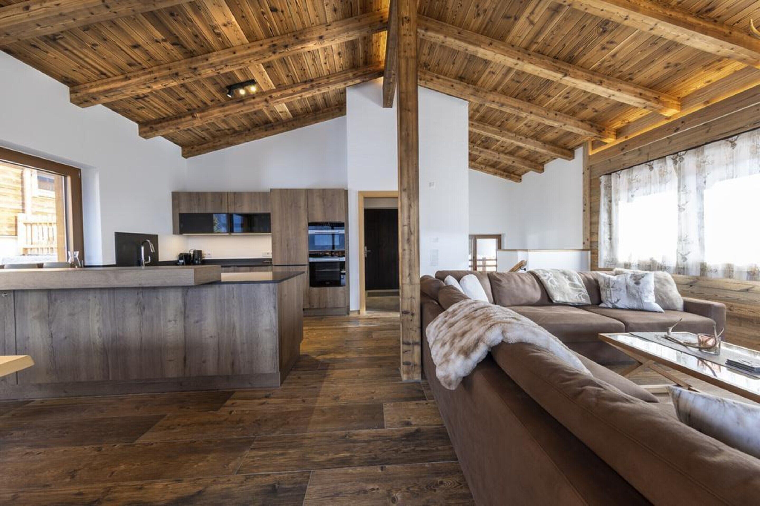 A spacious living area with a wooden ceiling, a large sofa, and a kitchen area with modern appliances.
