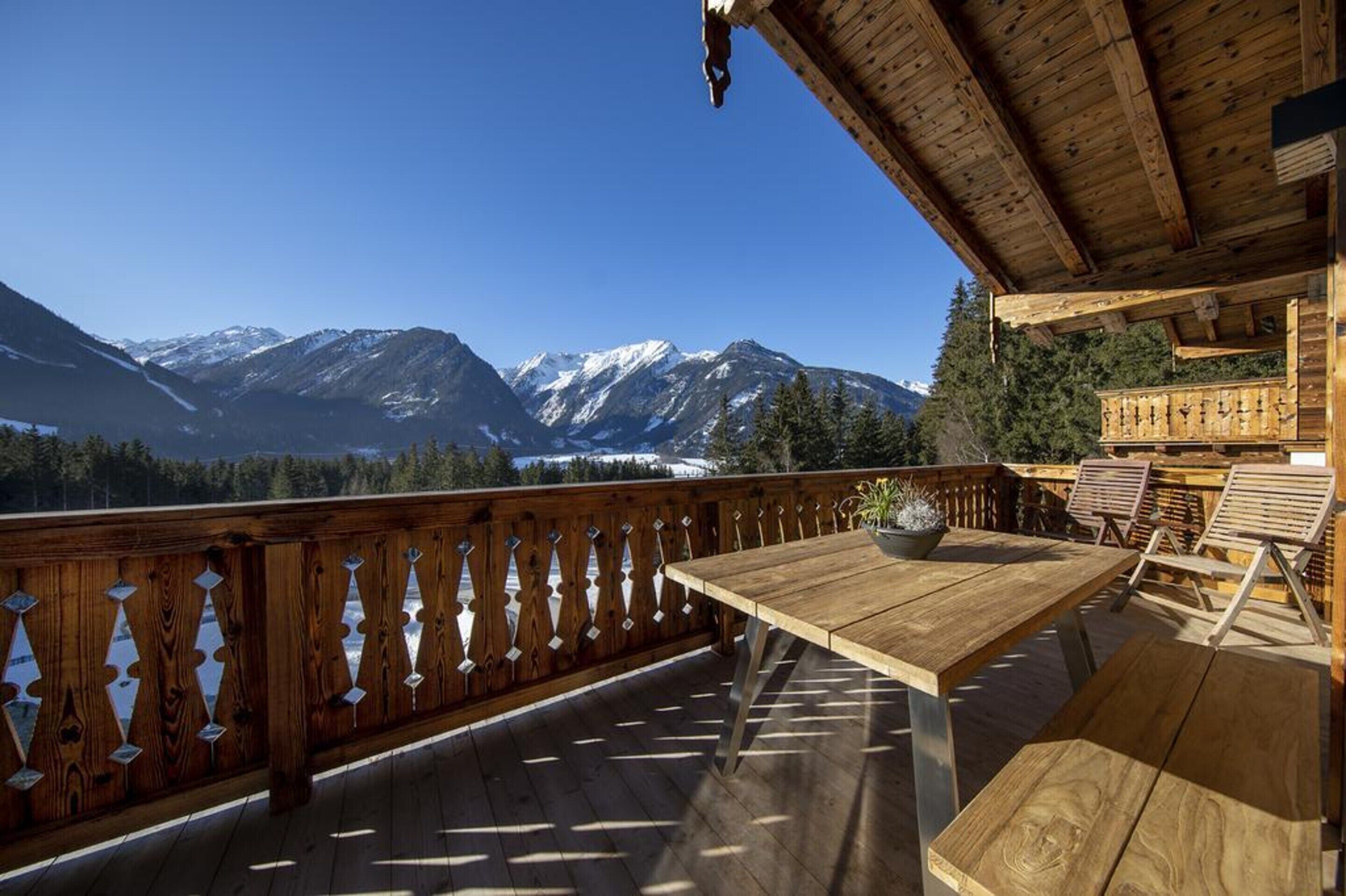 A wooden deck with a table and chairs, overlooking a mountainous landscape.