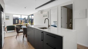 Eine moderne Küche mit einer großen Kochinsel, dunklen Schränken und Blick ins Freie durch große Fenster.