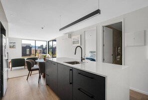 Eine moderne Küche mit einer großen Kochinsel, dunklen Schränken und Blick ins Freie durch große Fenster.