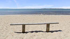 Una playa con un banco de madera en primer plano y un mar tranquilo al fondo.