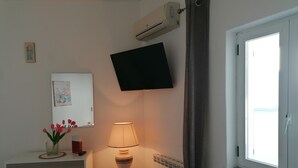 A bedroom with a bed, a bedside lamp, a TV mounted on the wall, a radiator, and a window with curtains. - APARTMENT IN QUIET AREA, MINUTES FROM SPA PARKS AND BEACH, (FORIO)