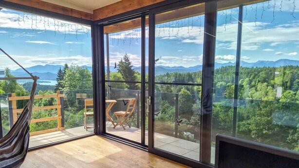 A room with large windows, a hammock, and a wooden floor.