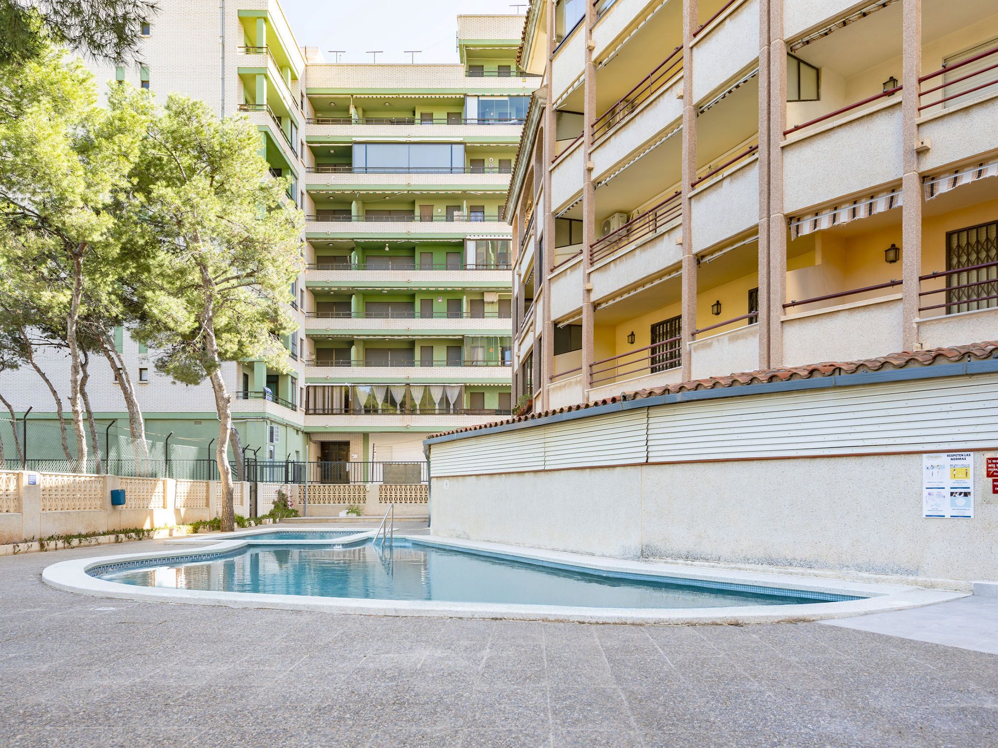 Un immeuble à plusieurs étages, avec une piscine en premier plan.