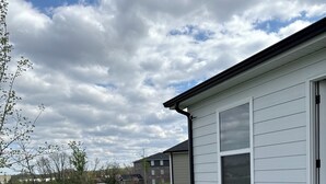 A backyard with a covered grill, a patio table, and a white building with shutters.