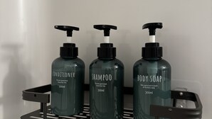 Three bottles of conditioner, shampoo, and body soap on a black shelf.