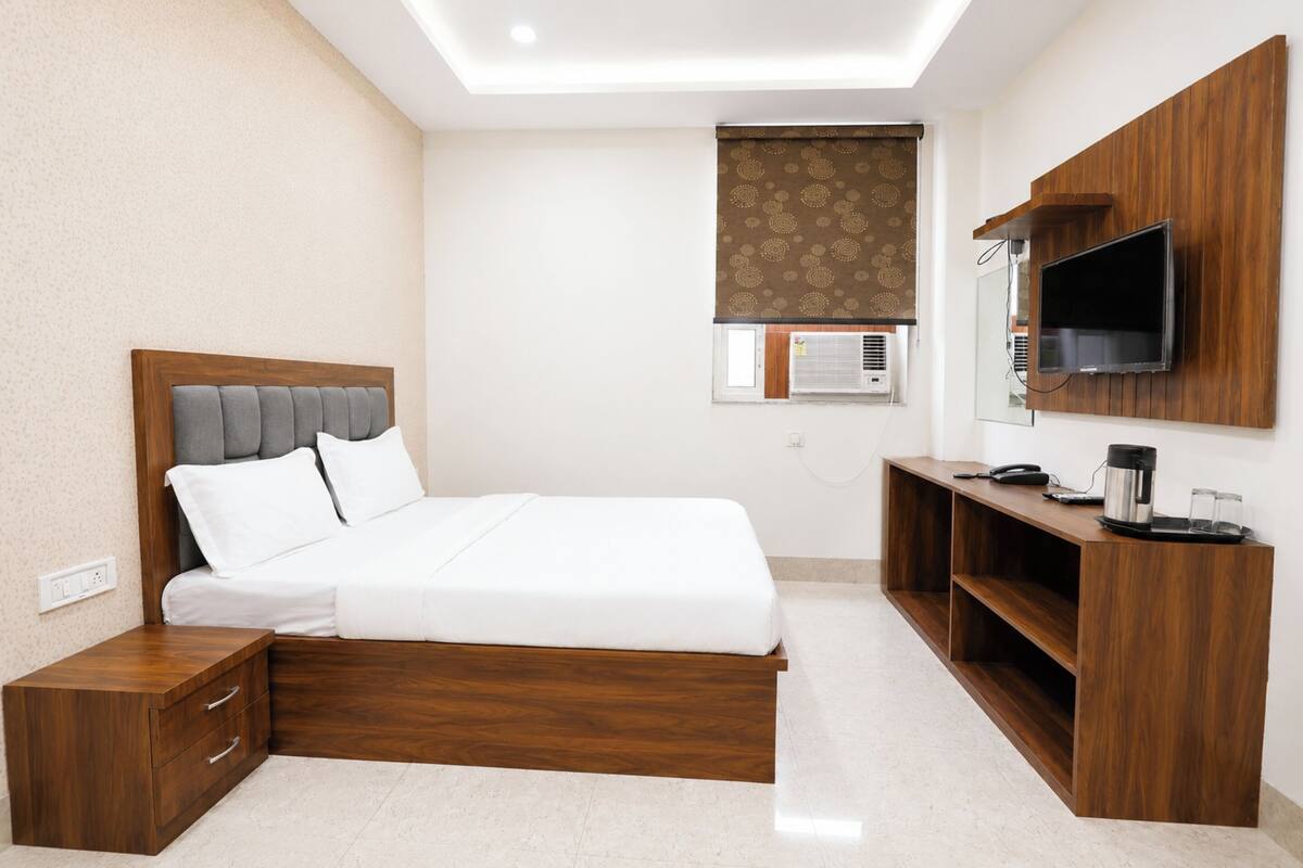 A bedroom with a bed, bedside table, TV, and a desk with a chair.
