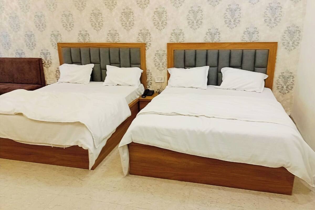 Two twin beds with wooden frames and grey upholstered headboards, white bedding, and a patterned wallpaper background.