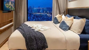 A hotel room with a large bed, a television on the wall, and a city view through the window. - ZENITY Skyline Residences Suite (Ho Chi Minh City)