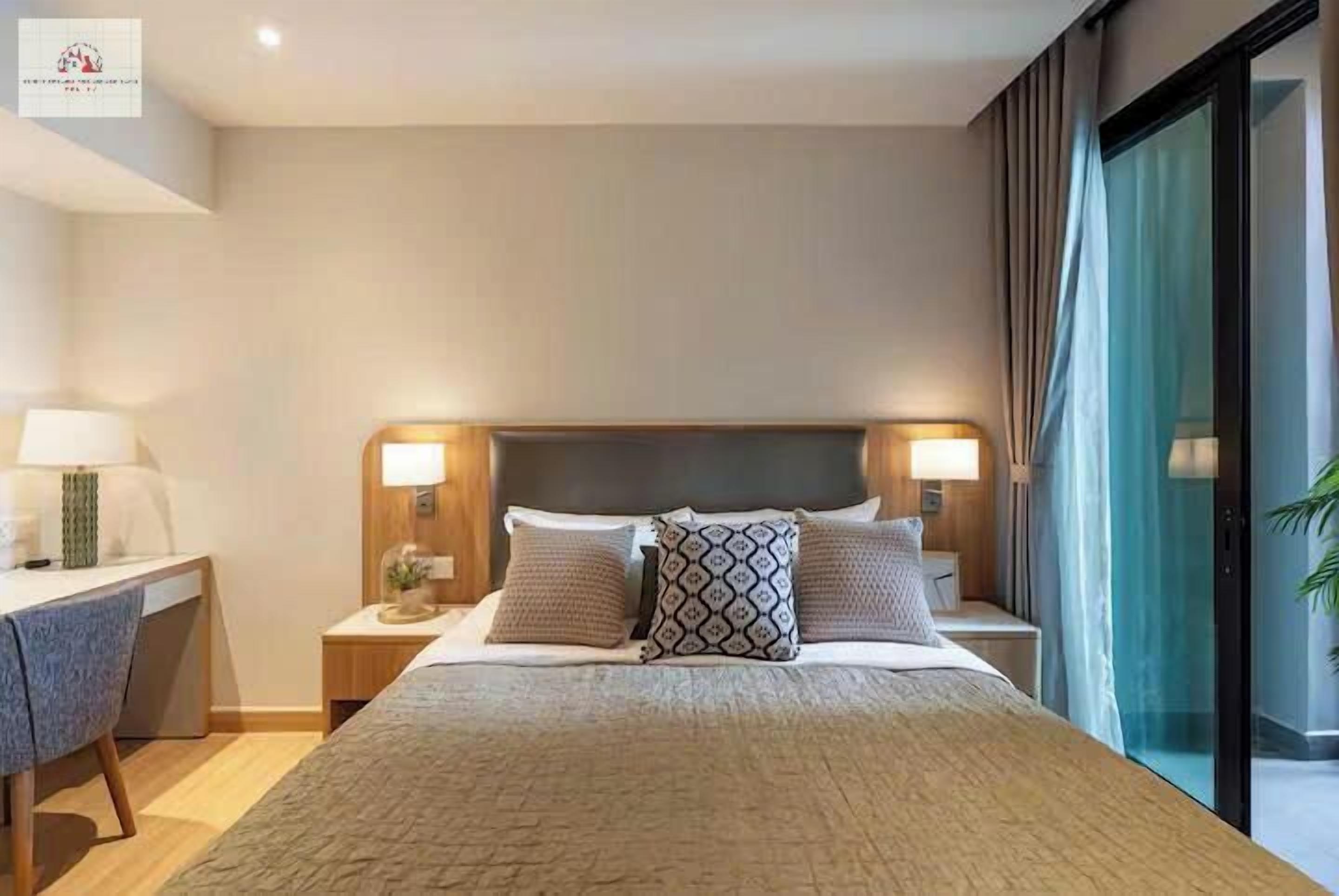 Habitación de hotel con una cama grande, dos mesitas de noche con lámparas, un escritorio con una silla y un amplio ventanal con cortinas.