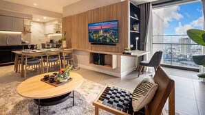 A modern living room with a dining area, a TV mounted on the wall, and a large window offering a city view. - ZENITY Skyline Residences Suite (Ho Chi Minh City)