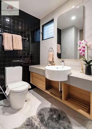 Un baño moderno con inodoro, lavabo y espejo. Hay toallas colgadas en la pared y una orquídea en maceta sobre el mueble.