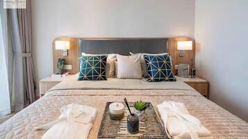 Quarto de hotel com uma cama grande, duas mesas de cabeceira, uma cabeceira e um porta-bandeja com toalhas e um vaso.