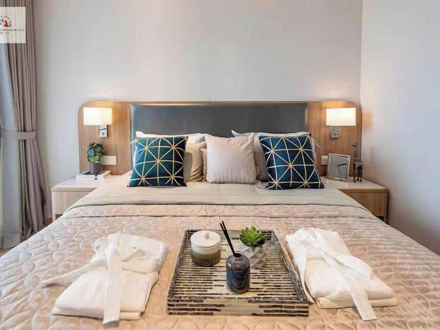 Quarto de hotel com uma cama grande, duas mesas de cabeceira, uma cabeceira e um porta-bandeja com toalhas e um vaso.