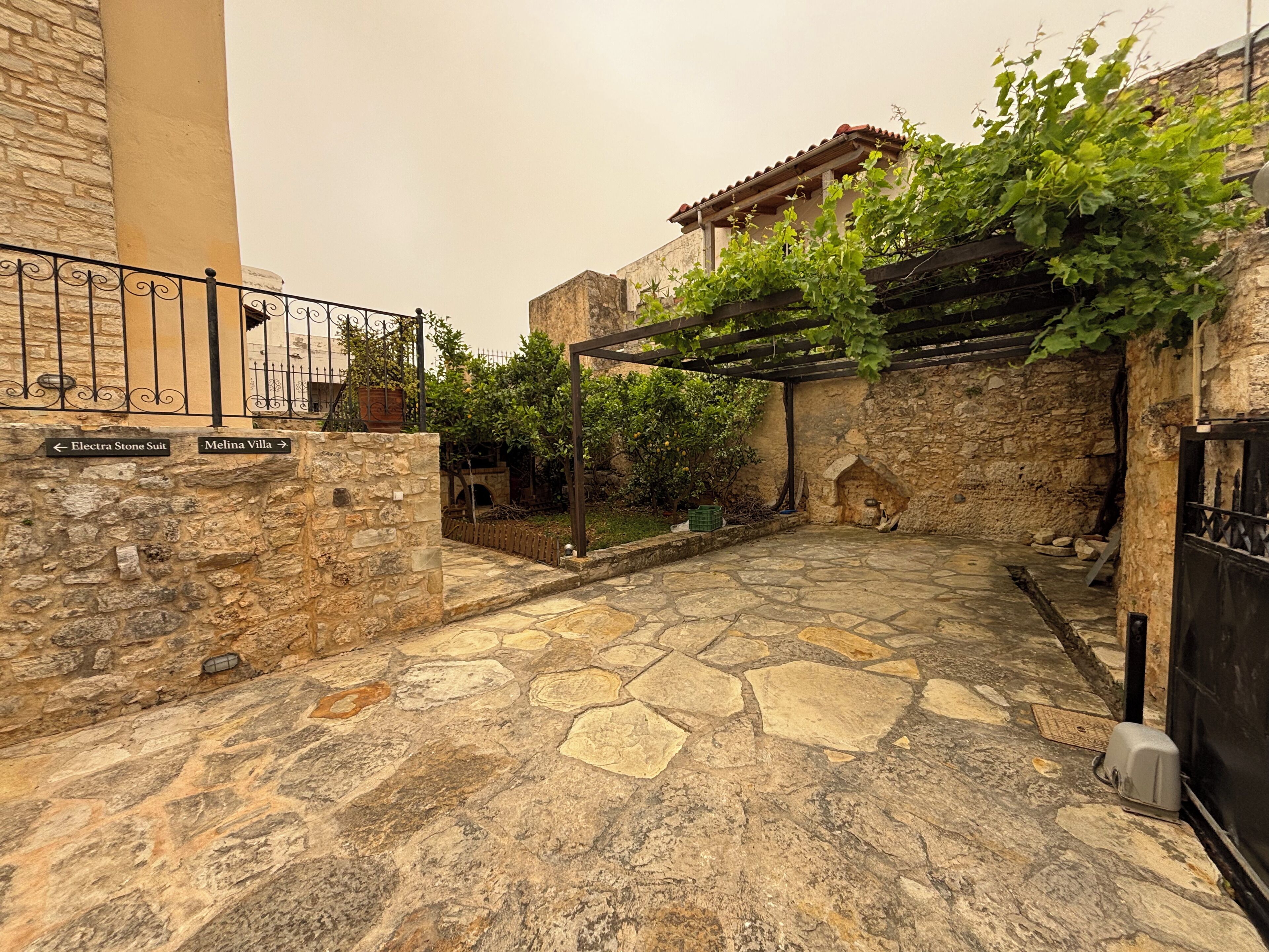Ein Innenhof mit Steinpflaster, einer Pergola mit Kletterpflanzen und einer Steinmauer mit Beschilderung.