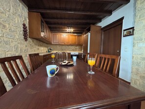 A wooden dining table with chairs, a glass of orange juice, and a mug. - Melina Stone Villa (Roumelí)