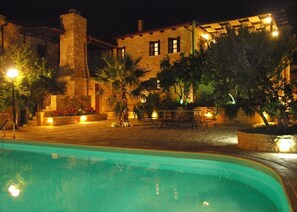 A pool area with a stone building in the background, surrounded by trees and outdoor seating. - Melina Stone Villa (Roumelí)