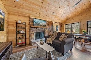 L’intérieur chaleureux d’un chalet avec une cheminée en pierre, des murs en bois, un canapé et un coin repas.