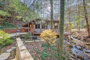 Une cabane avec une terrasse, un petit porche et un ruisseau.
