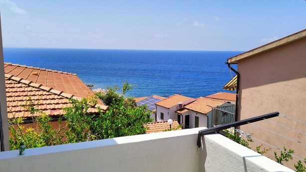 A view of a coastal town with terracotta-roofed buildings, a clear blue sea, and a balcony with a railing. - Il Gelso - Sea View Holiday Home in Pomonte - Elba Island (Pomonte)