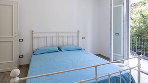 A bedroom with a bed, white walls, and a balcony with a view of greenery. - Il Gelso - Sea View Holiday Home in Pomonte - Elba Island (Pomonte)