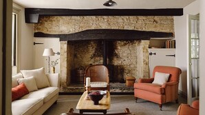A cozy living room with a stone fireplace, a sofa, a chair, and a table with a candle and a bowl of fruit. - Spacious Country Farmhouse in Rewilding Landscape (Mapperton)