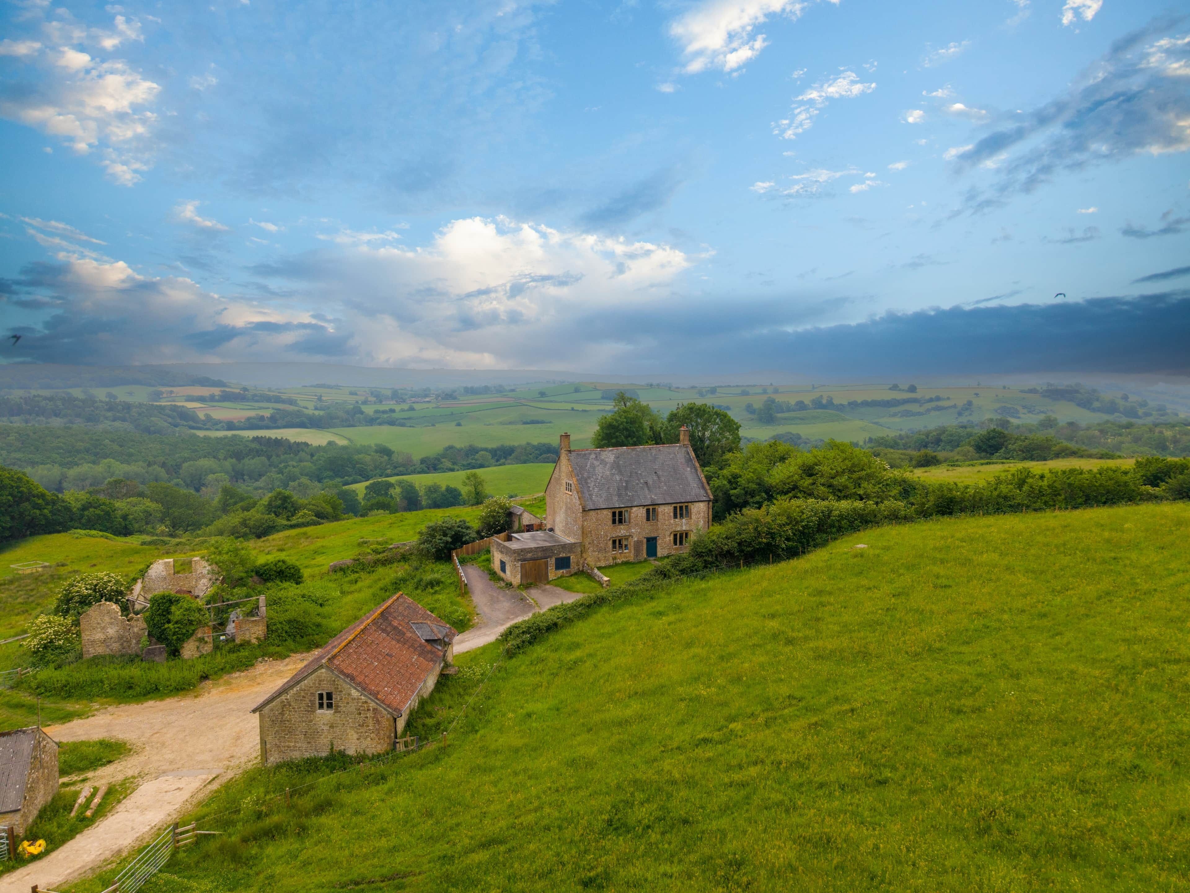 Un paysage rural avec une maison en pierre, un bâtiment plus petit et un chemin menant à la maison.